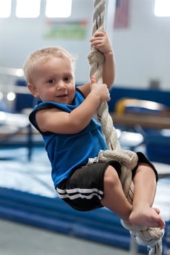 Toddler in a blue shirt at gymnastics class climbing a rope with large knots