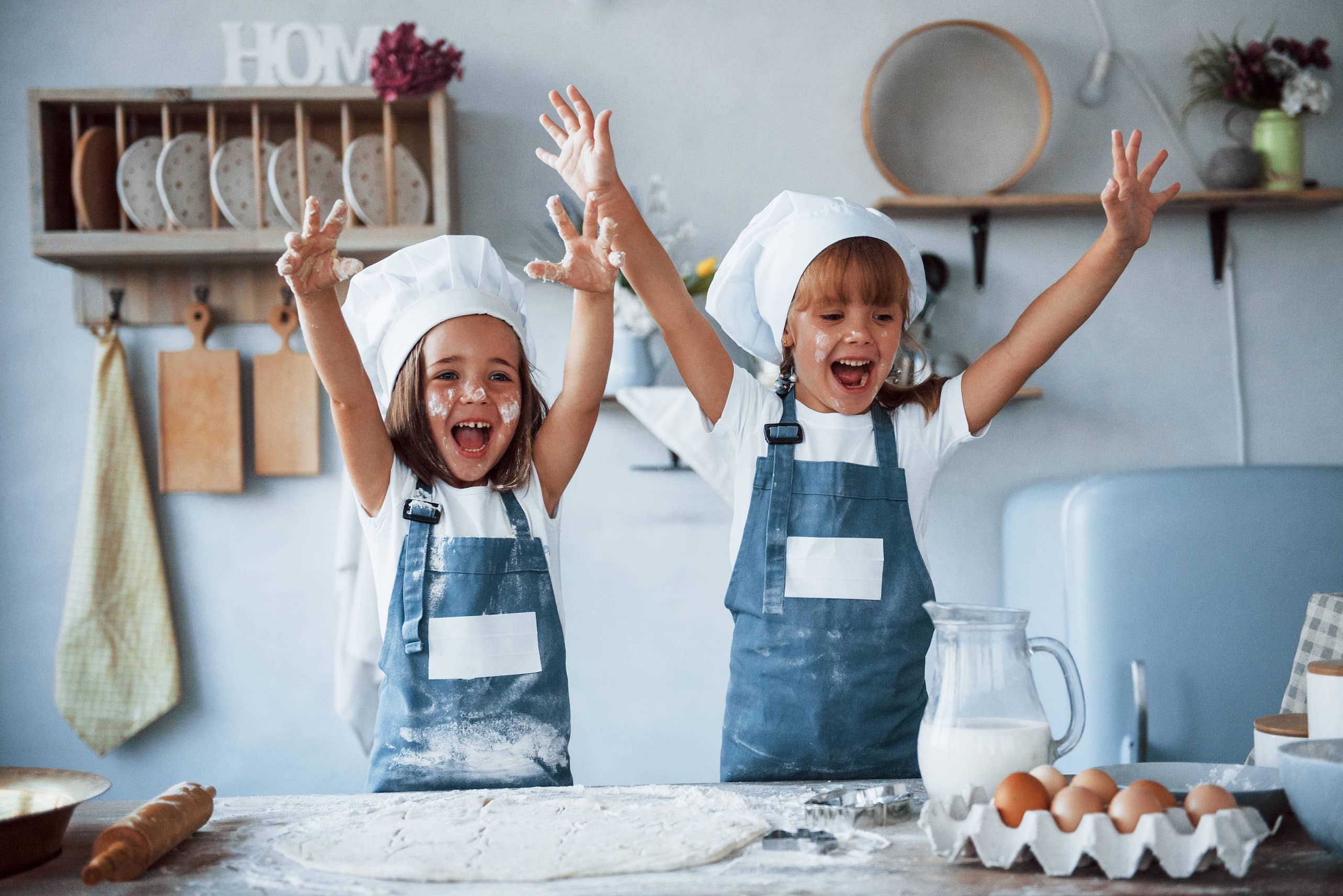 Two sisters baking in the kitchen with baker's hats and flour on their faces.