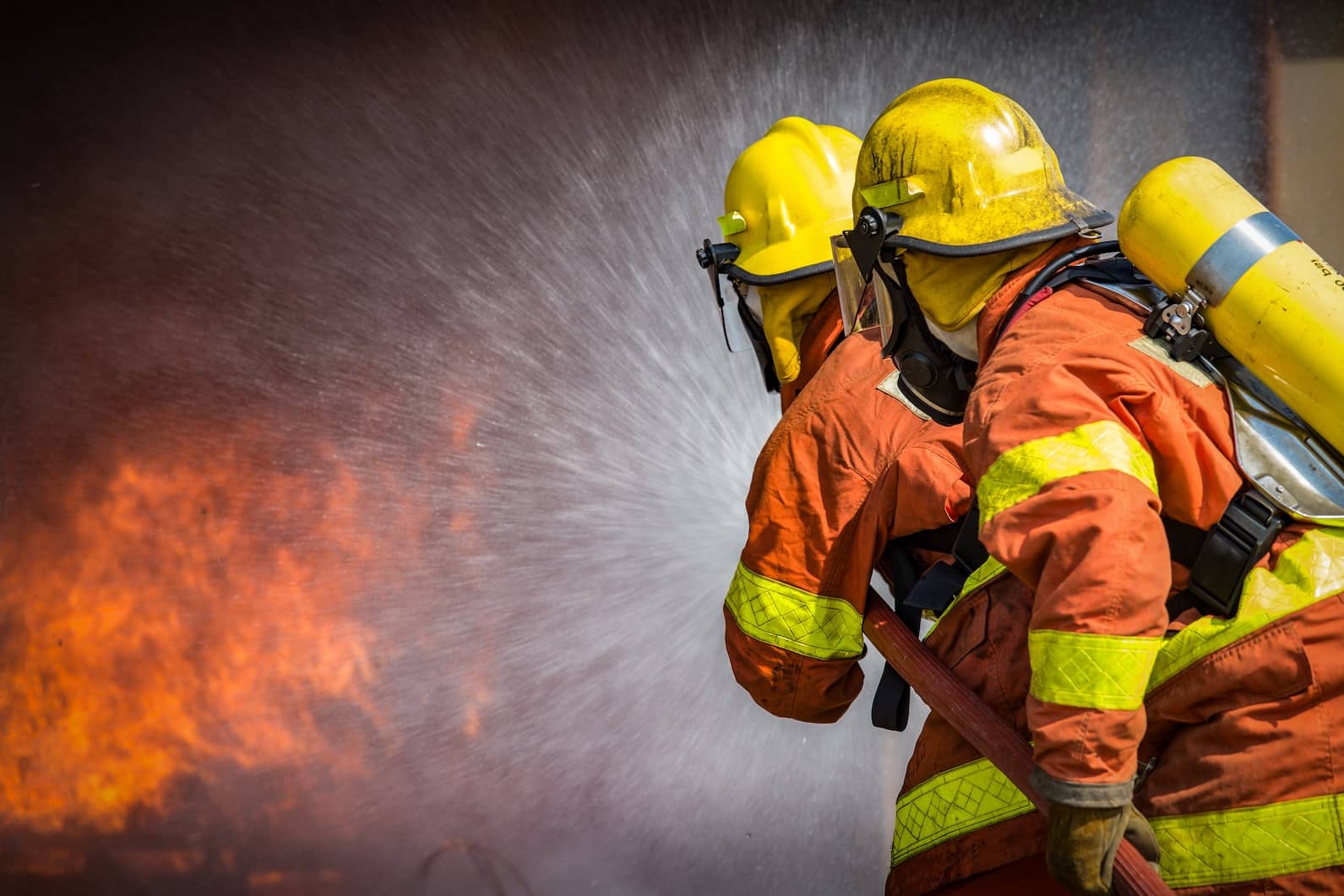 Two firefighters spray high pressure water while fighting a fire.