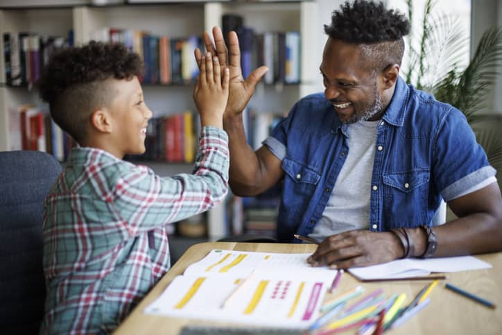A black father high-fiving his son when he finished his homework.