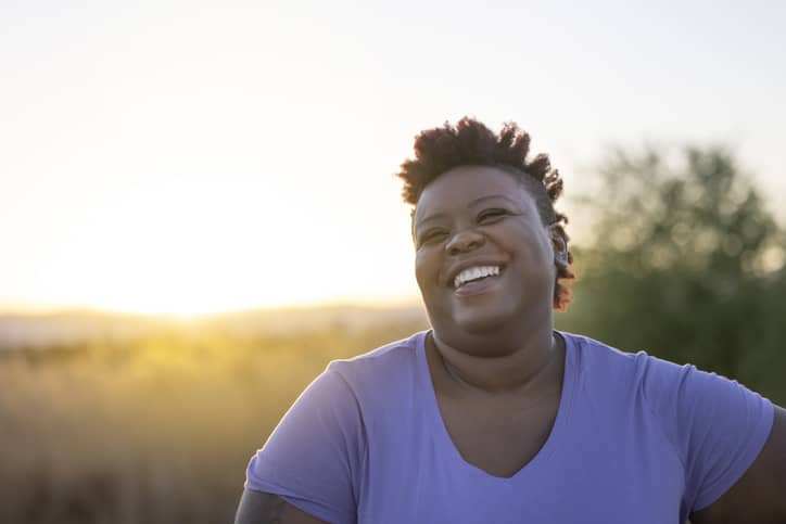 A black woman laughing after finishing a vigorous run with sunlight in the background.