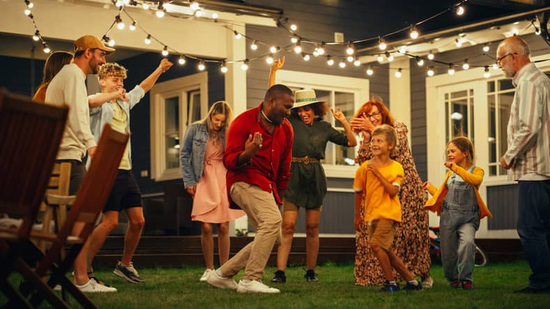A blended family having fun and dancing with friends in a light-up backyard.
