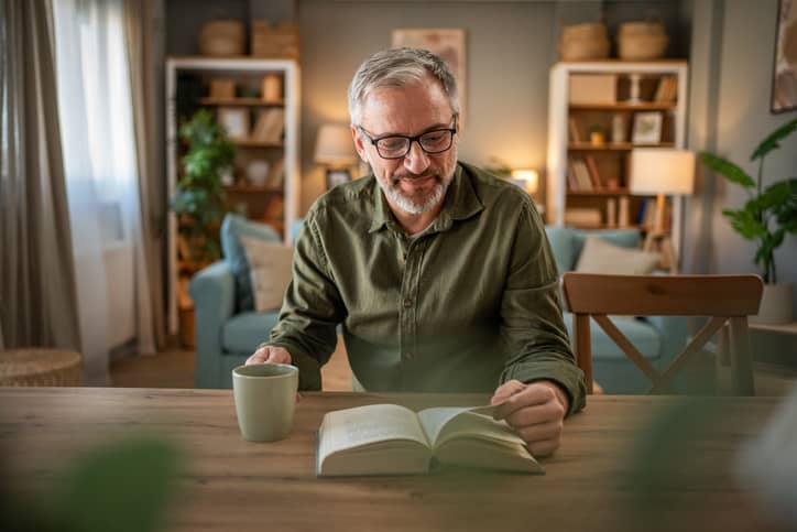 A mature man reading a book on emotional intelligence while drinking coffee..