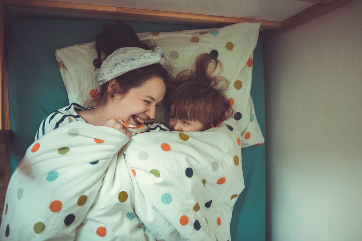 A young boy and his mother snuggling and hiding under a polka dotted blanket.