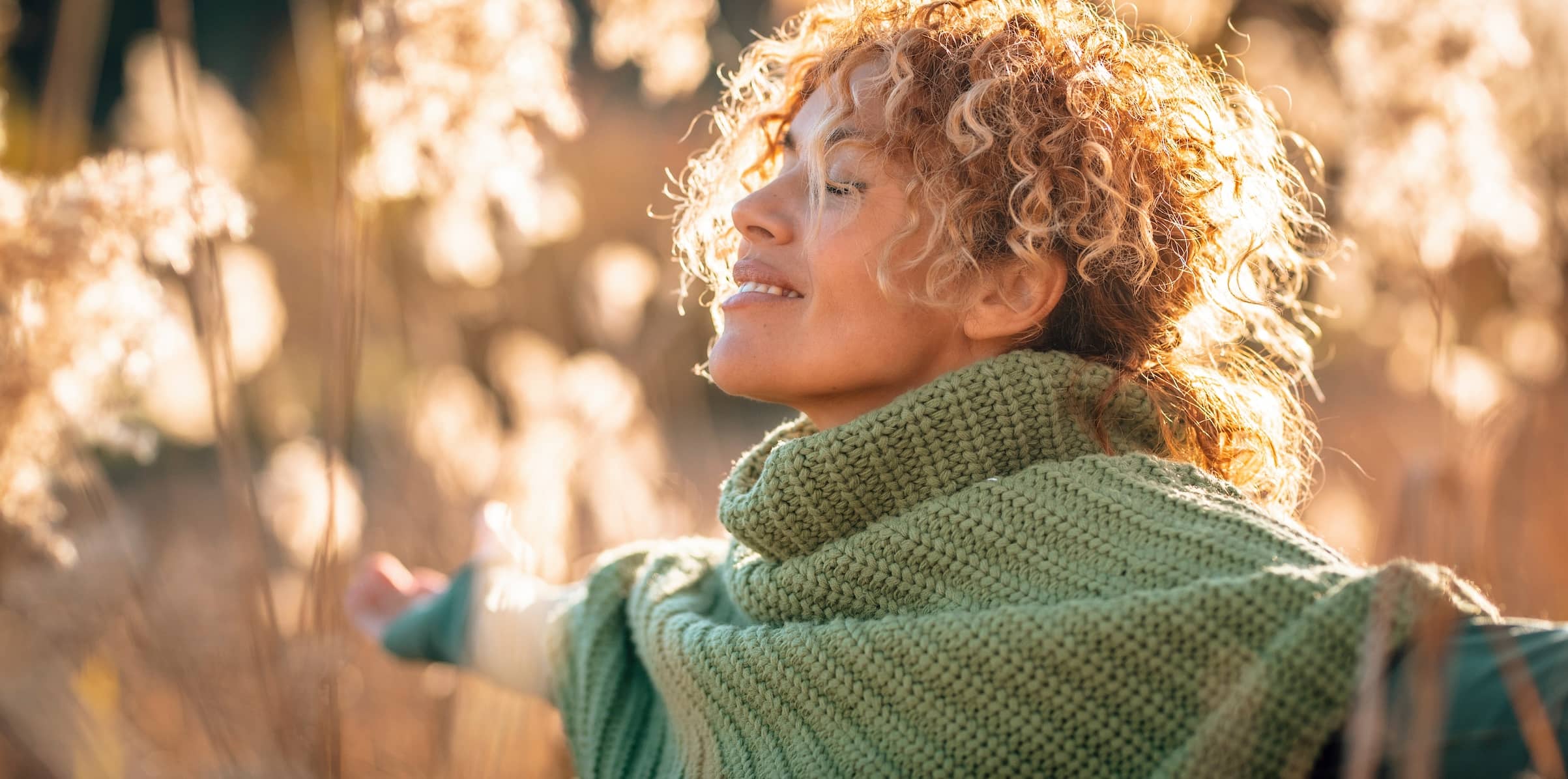 A young woman mindfully stretching her arms out while taking in the sunset light and breathing deeply..