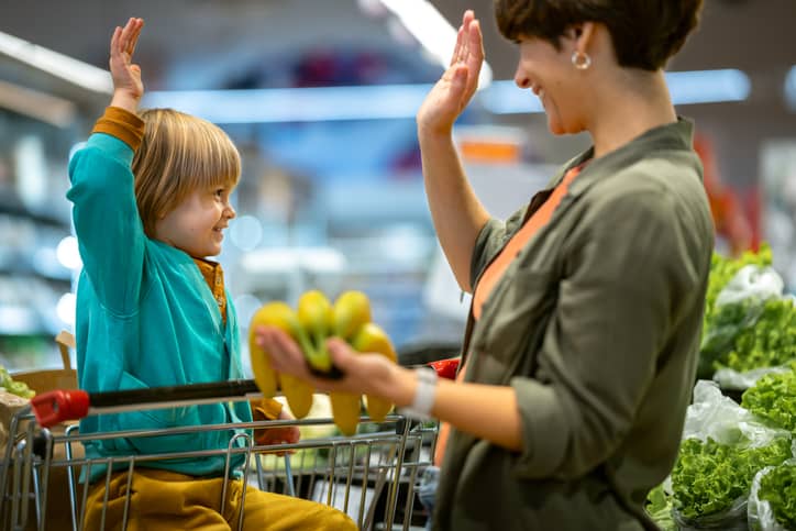 A mother with a child in a grocery store high-fiving.