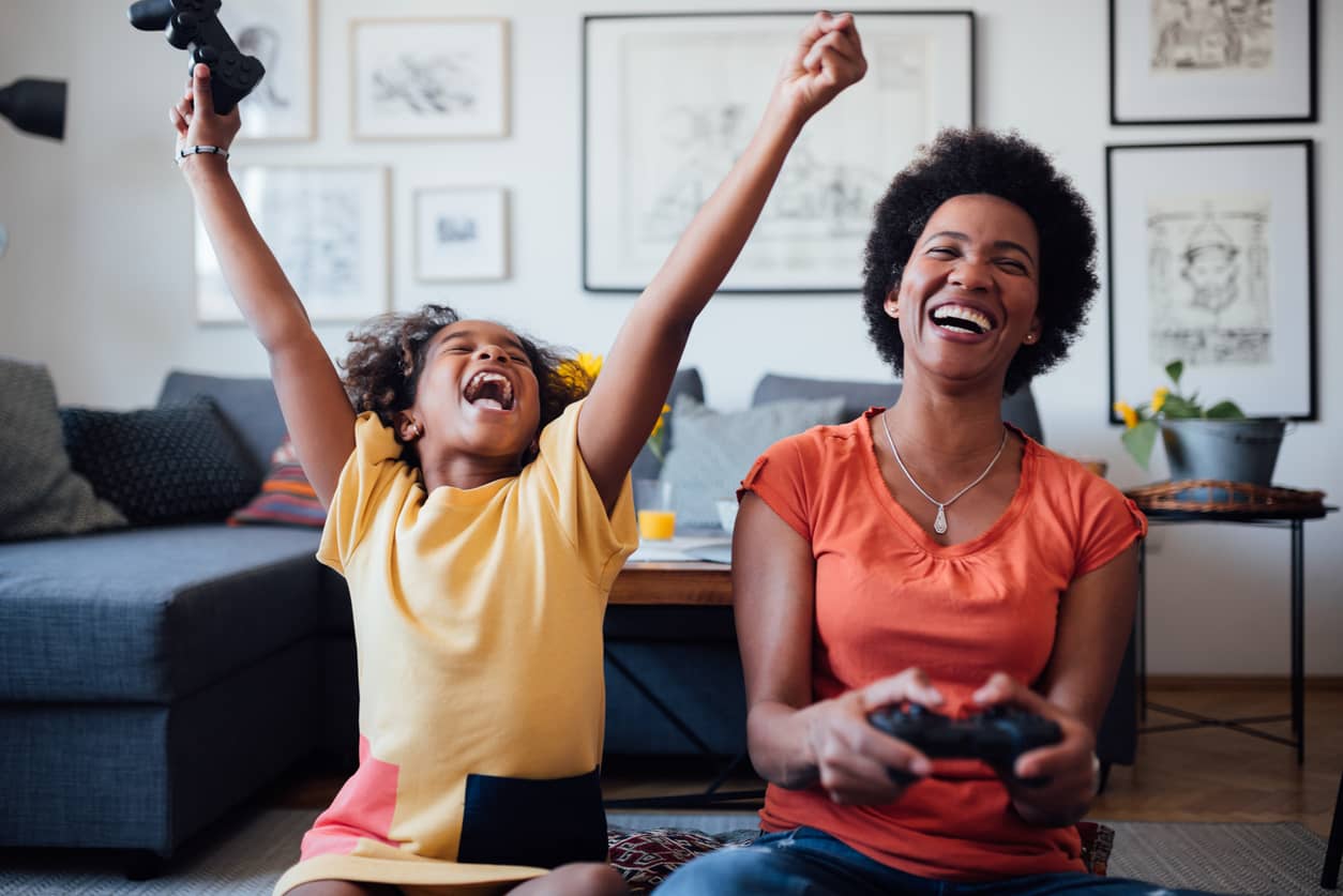 African American mother and daughter having fun playing video games at home.
