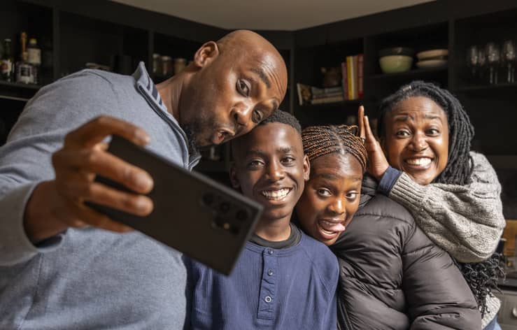 A black family taking a funny-faced selfie at home.