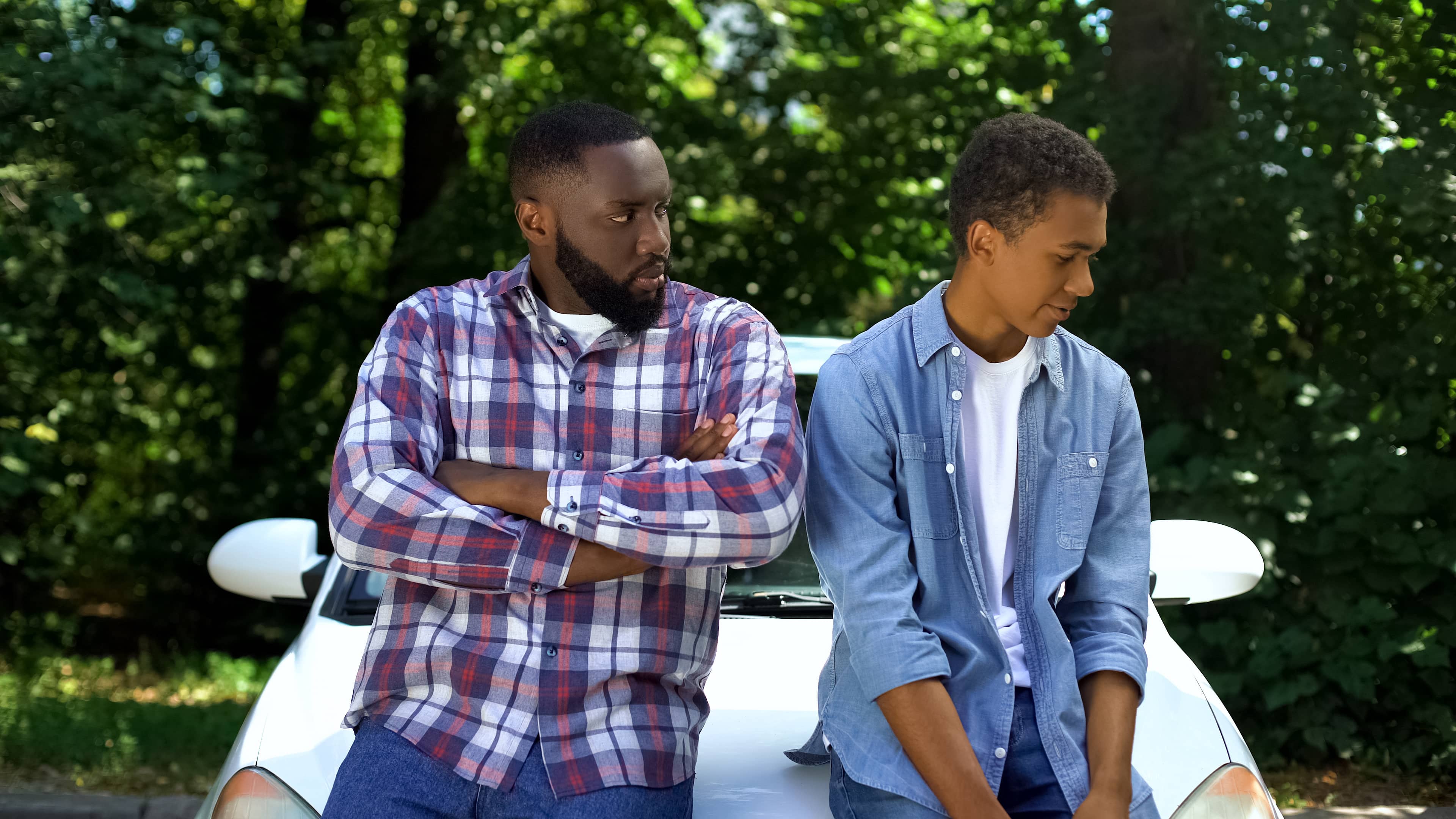 Angry father looking at guilty teen son near car. Healthy boundaries sometimes invoke intense feelings. 