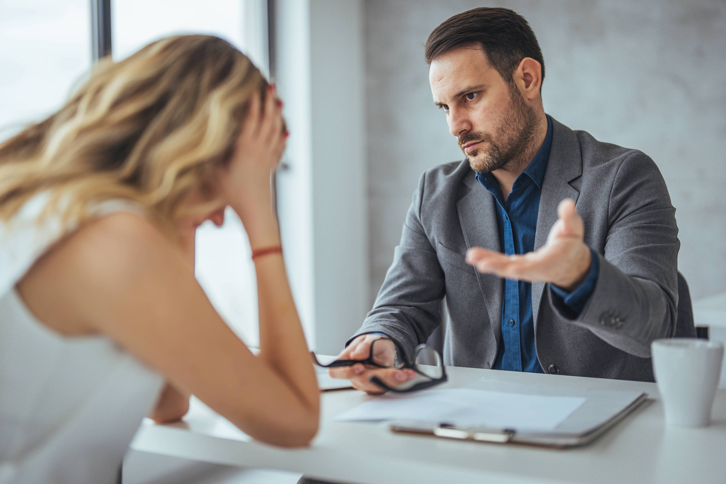 Angry businessman arguing with a businesswoman who has her head down indicatiing shes discouraged