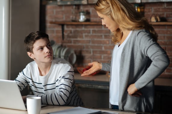 Teenager at a computer while engaging his mother