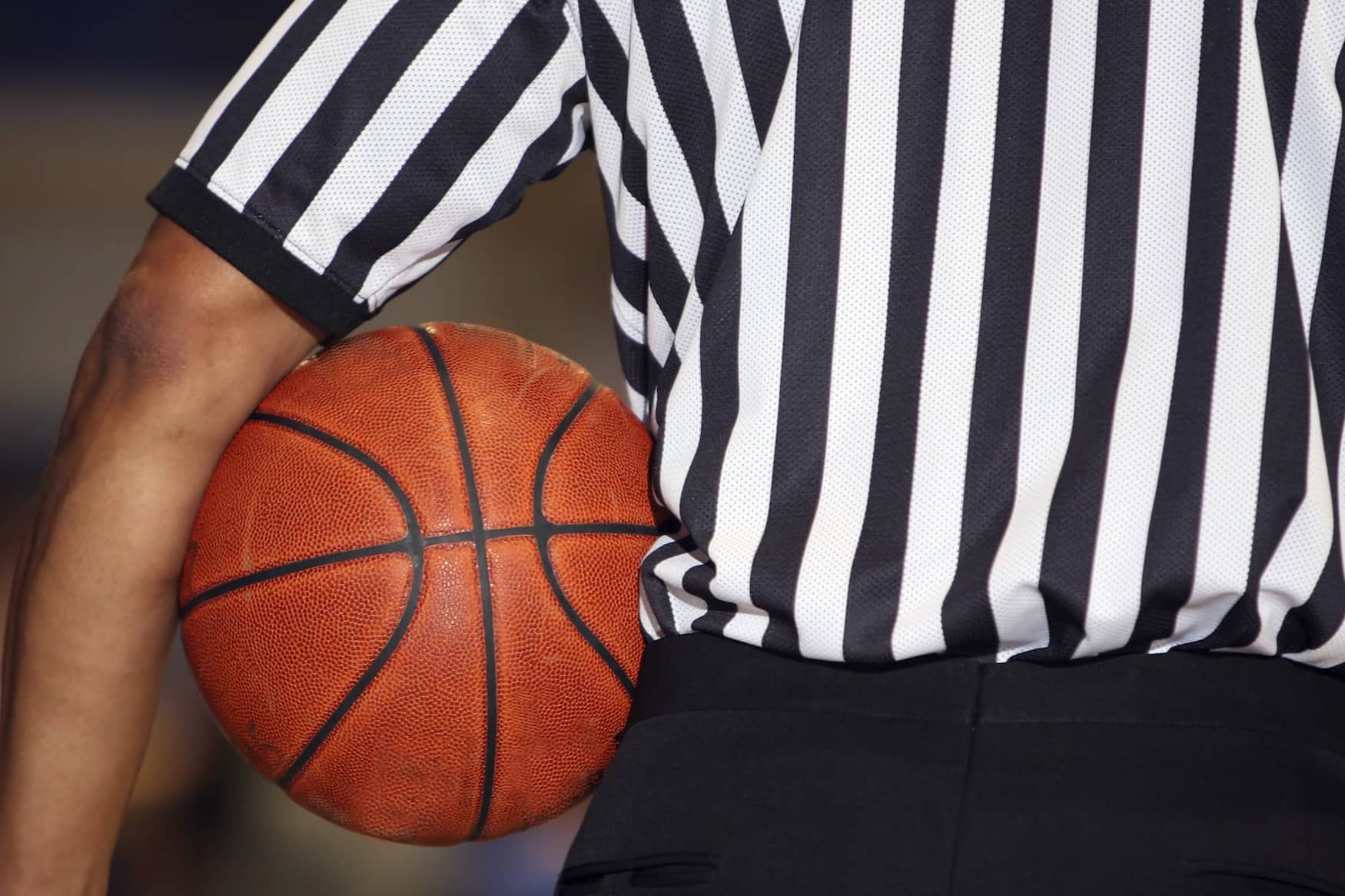 A basketball referee with a basketball held under his arm.