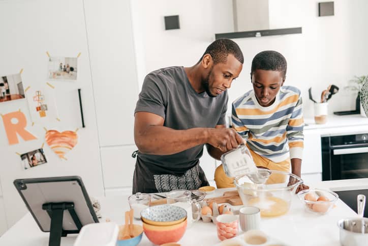 Father in the kitchen baking with his teen son teaching responsibility and contribution.