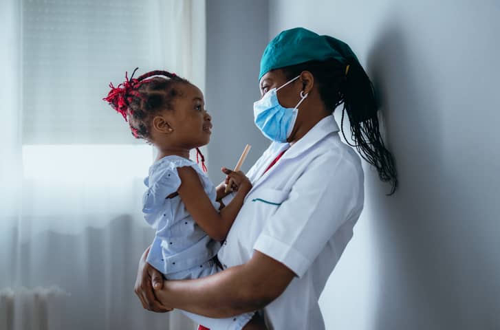 A young nurse in a hospital room holding a child while empathizing.