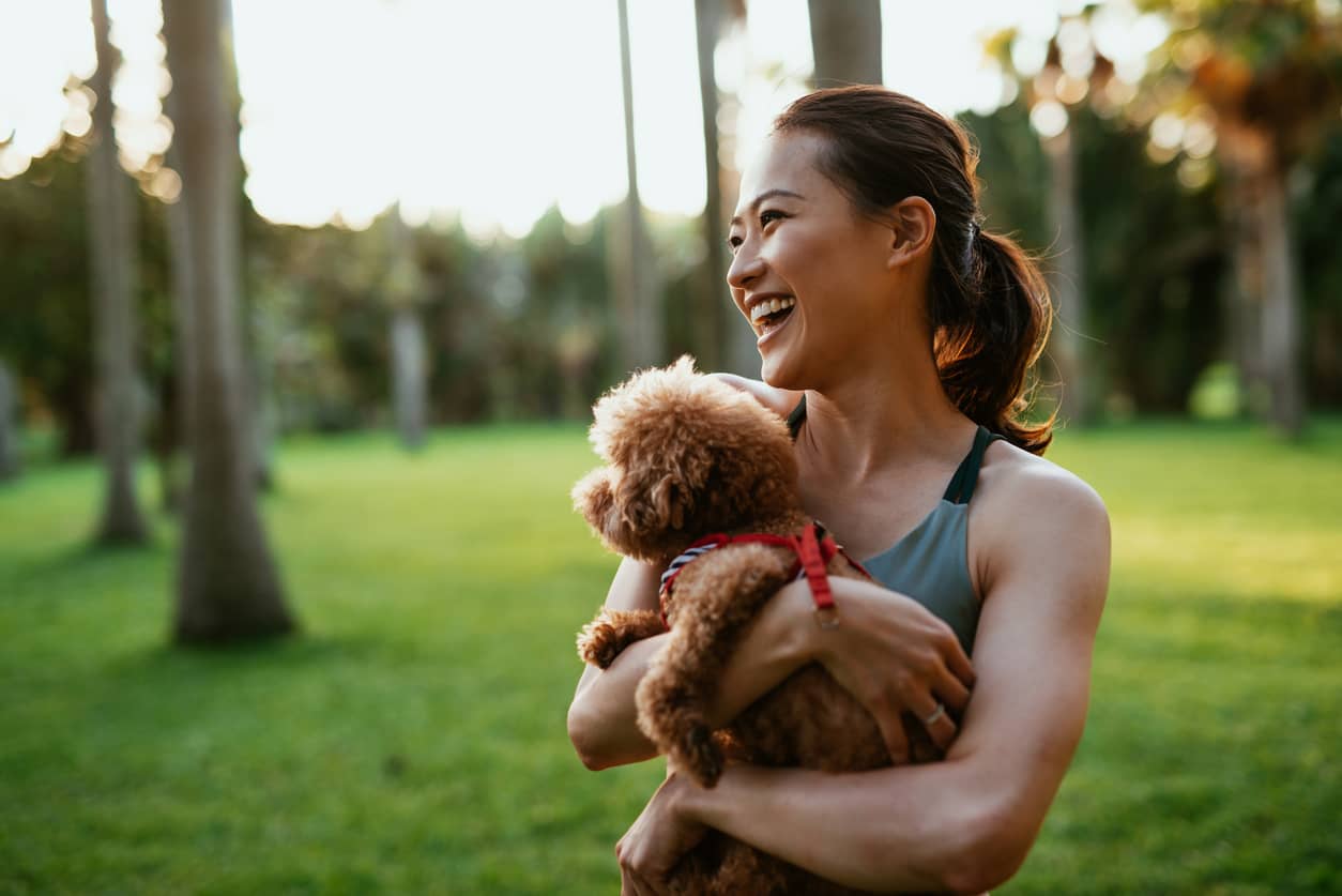 A beautiful Taiwanese woman holding her brown Maltese dog in the city park.