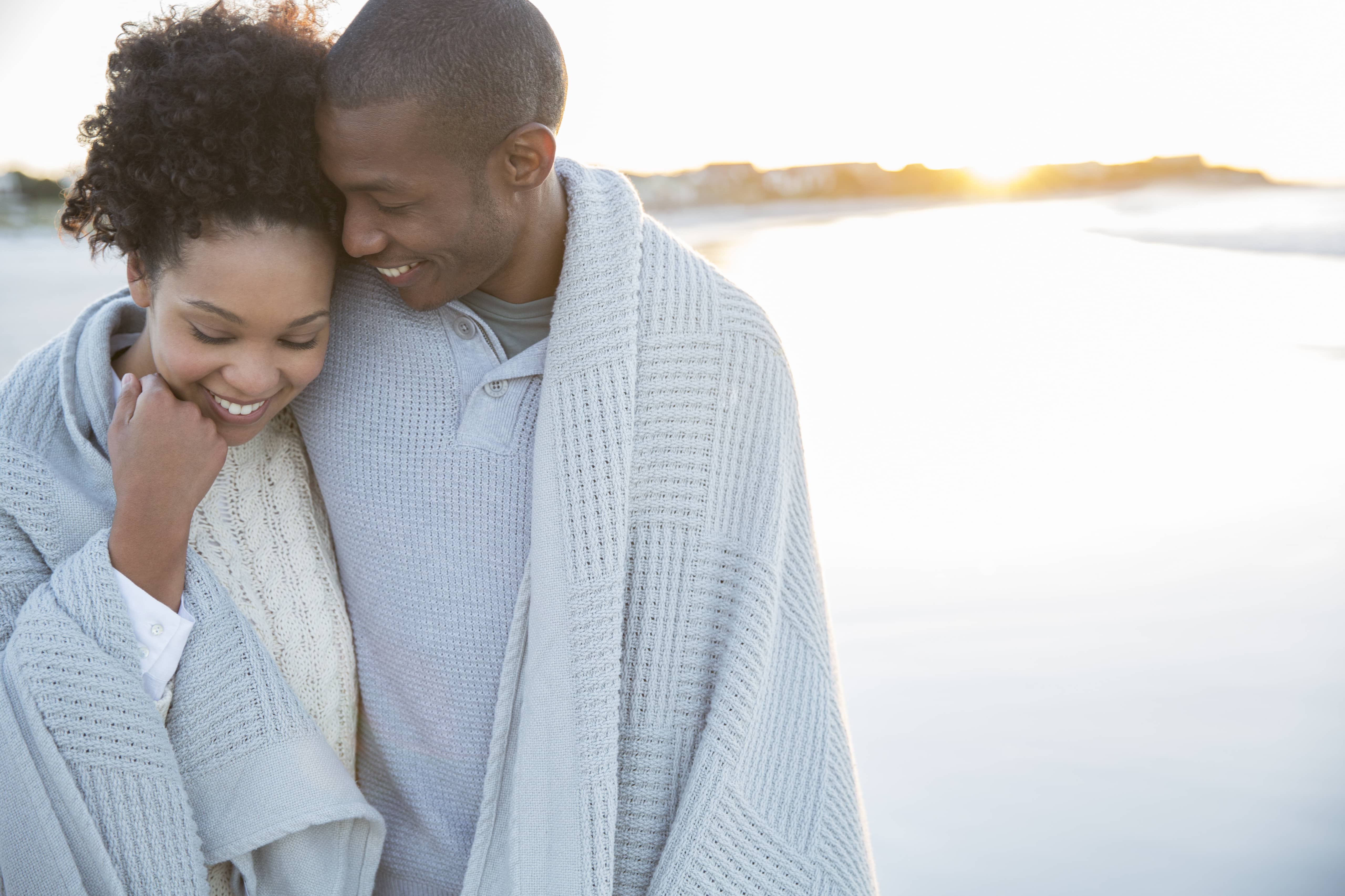 Black couple snuggling in a blanket by the ociean