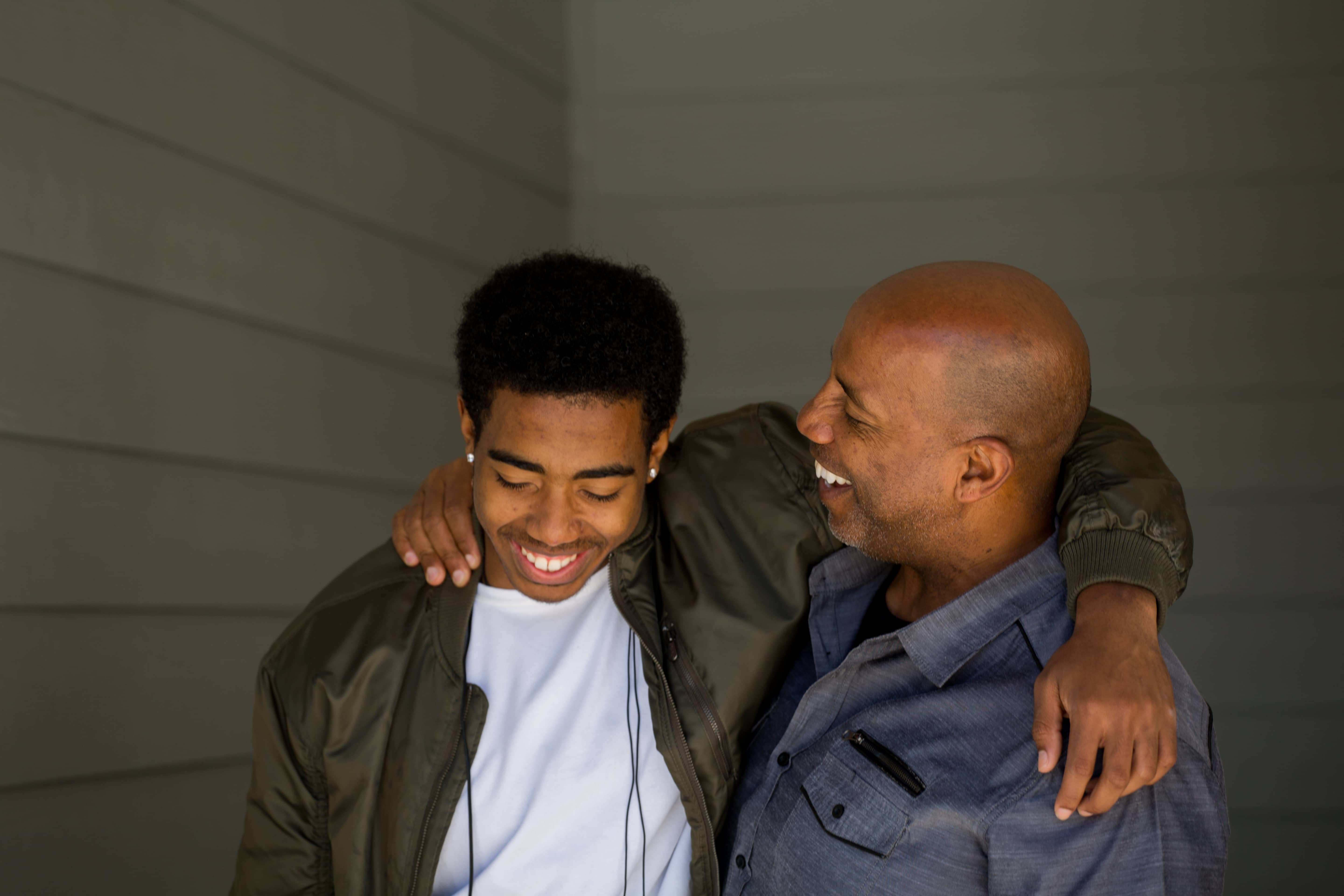 Black dad embracing and laughing with his teenage son.