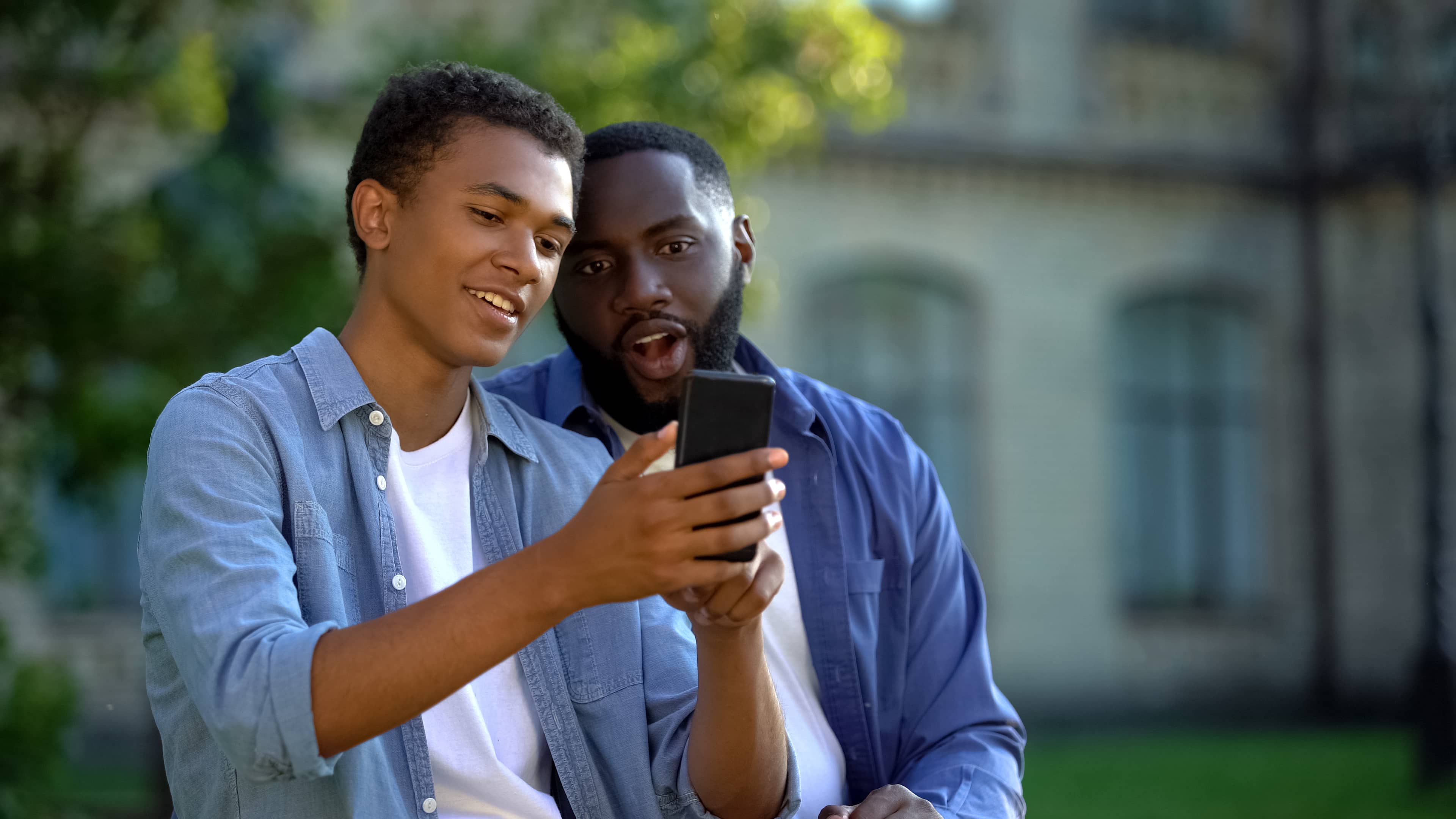 Black teenage boy showing his father a video on his smartphone