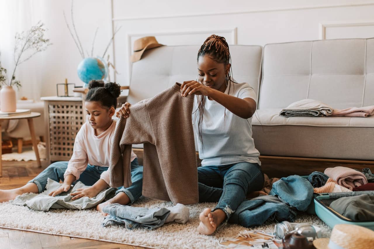 Black woman folding laundry with a preschool child. Learning life skills begins at home!