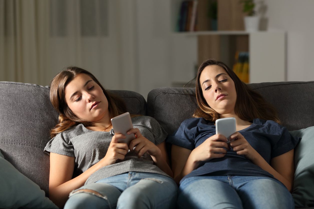 Two teenage girls on their smartphones ignoring each other.
