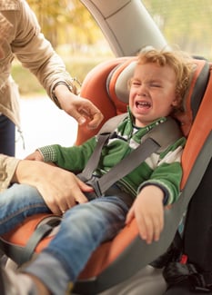 Unhappy toddler being buckled in a car seat