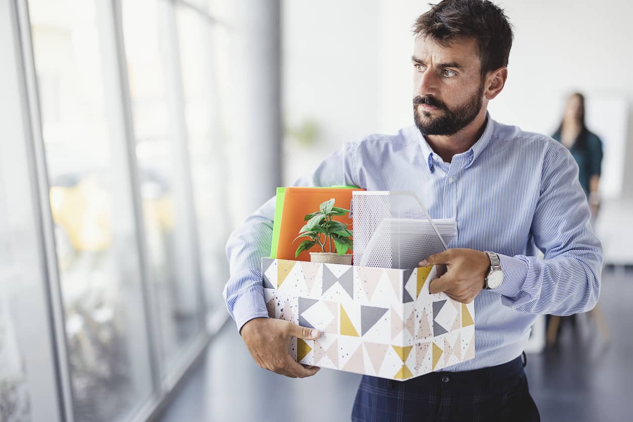 A business man carrying his belongings out of the office after a job layoff.