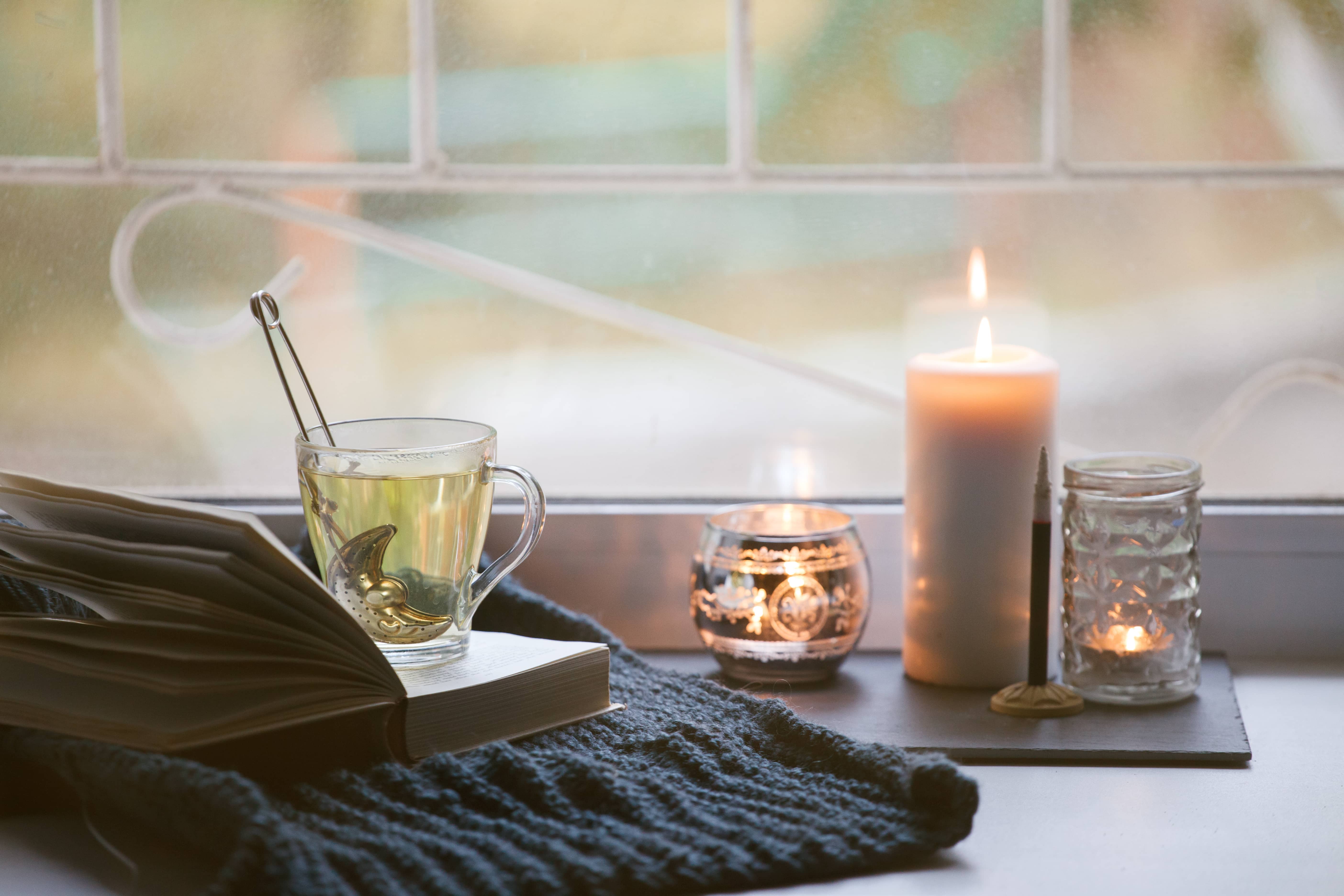 A beautiful lit candle, book and tea reading for a mom's self-care!