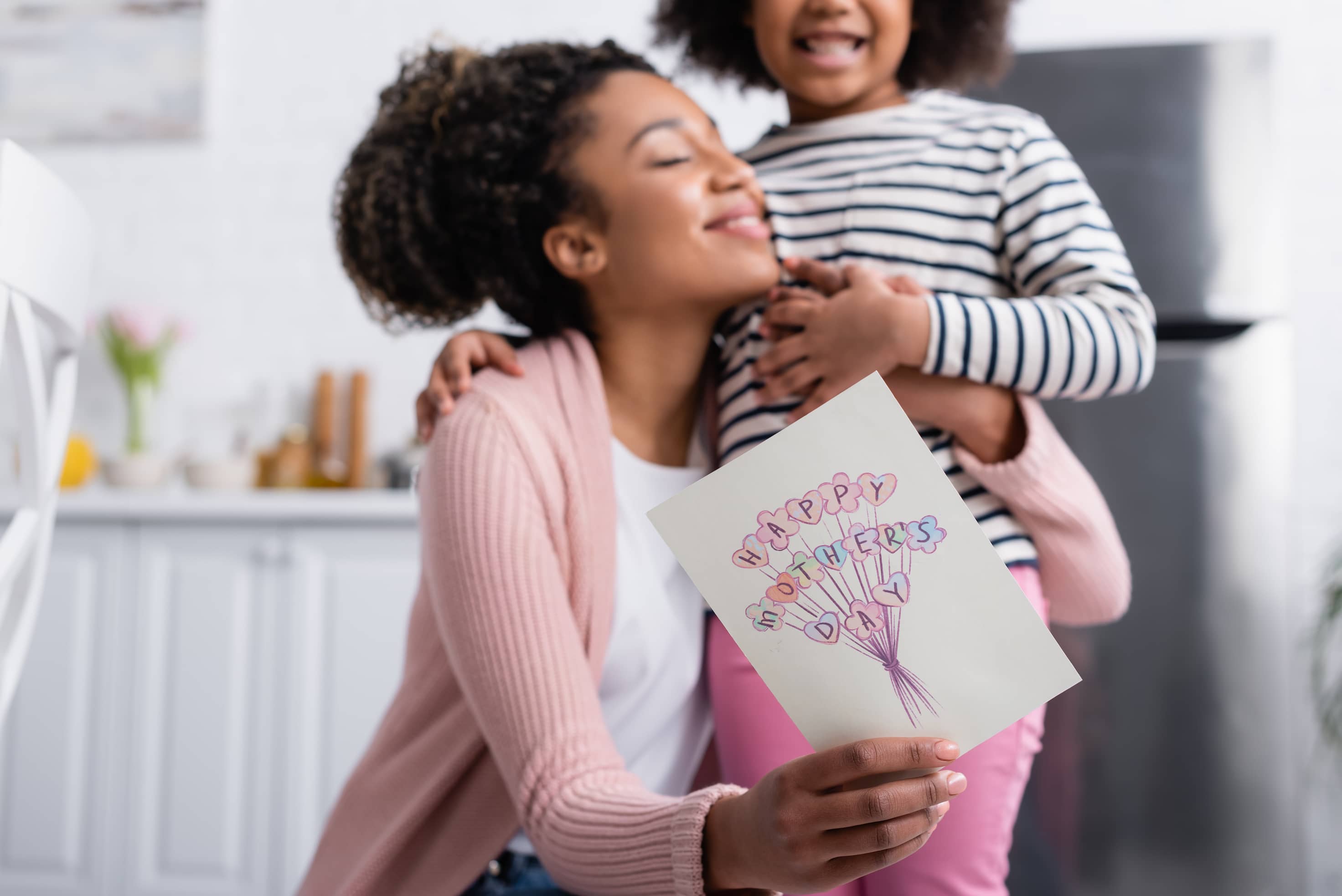 Cheerful African American showing Mother's Day card while hugging her daughter