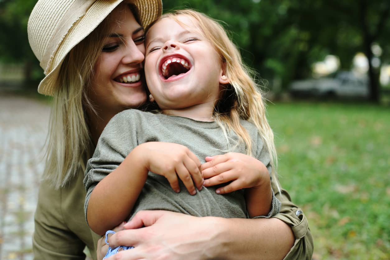 A Gentle Parenting Style mother embracing her preschool daughter outdoors.
