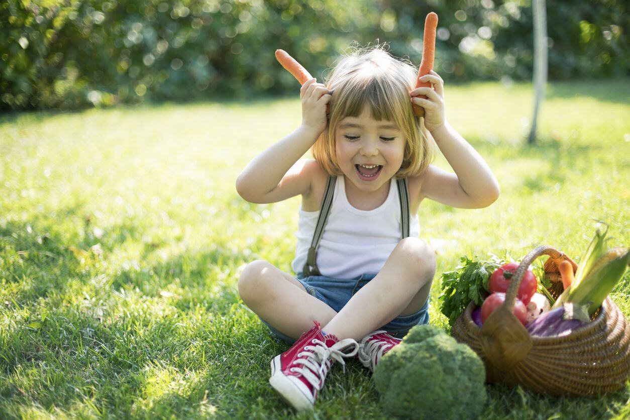 Child with a basket of organic vegetables pretending to be a bunny using carrots for ears as an example of free-range parenting style