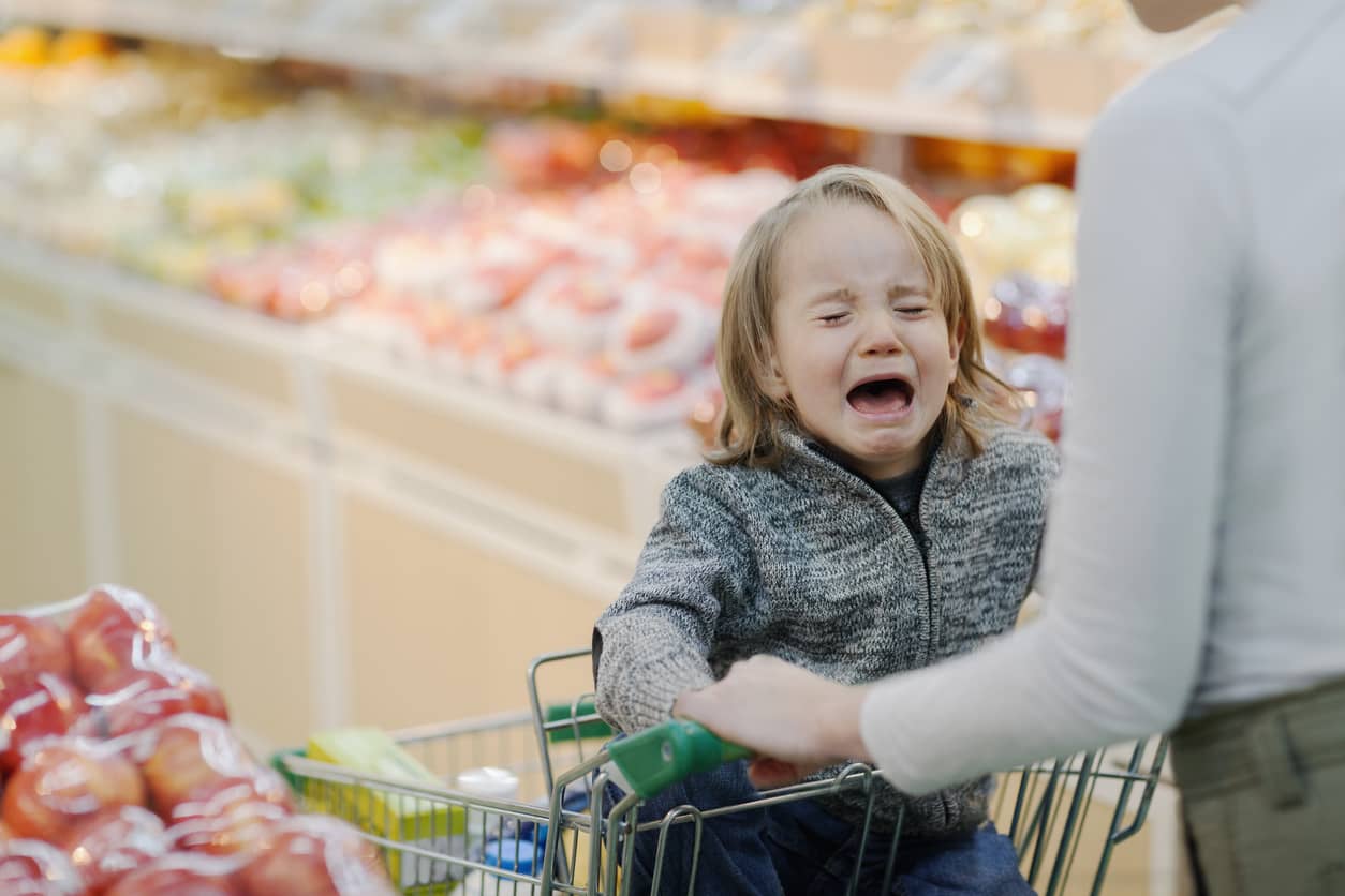 A child crying for candy in a shopping cart