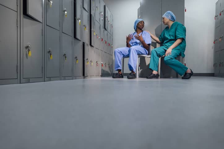 Fellow nurses talking while sitting on the floor in the locker room after a rough day in patient care.