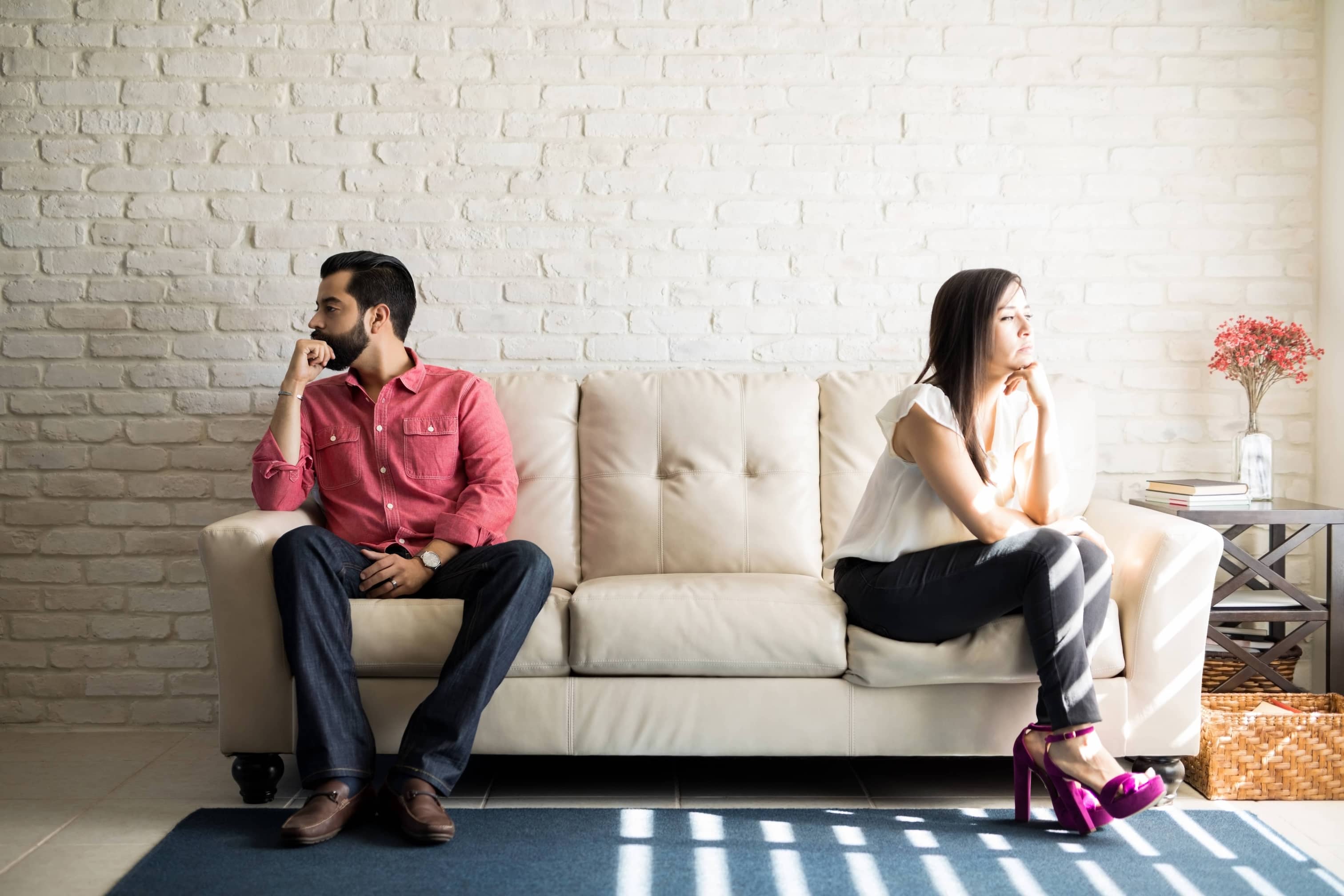 A couple distancing and facing away from each other on a beige couch.