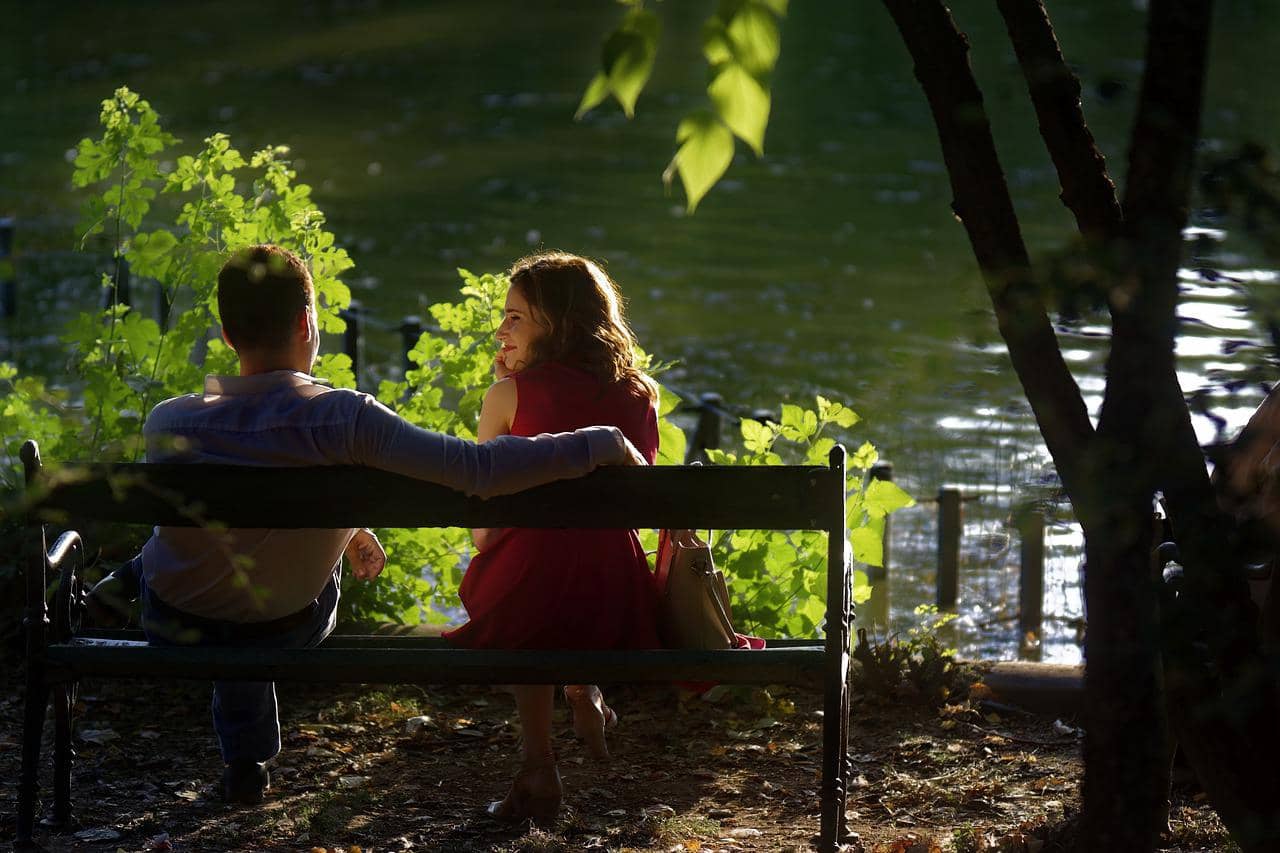 A loving couple sitting on bench at the edge of a lake.