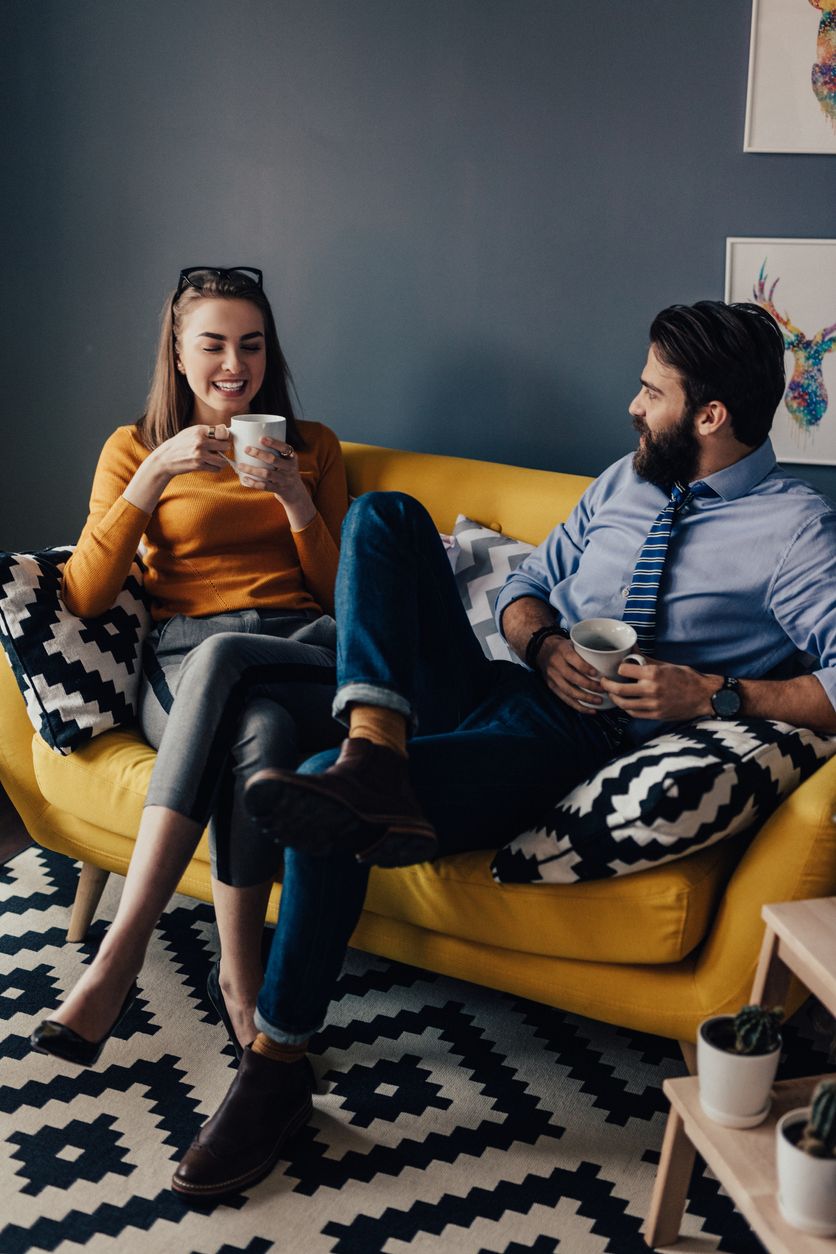 Couple sitting on a loveseat drinking tea and conversing.