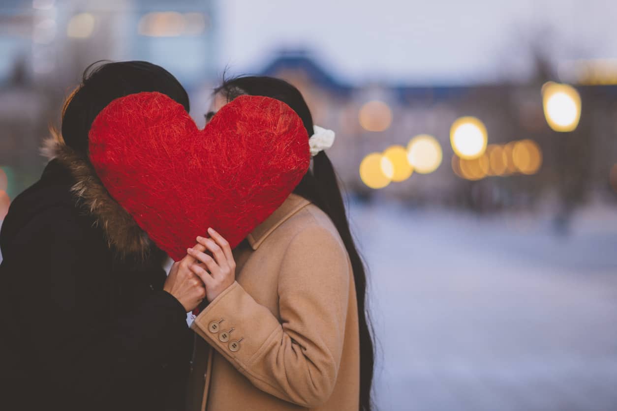 A couple hiding behind a giant heart on the streets of New York