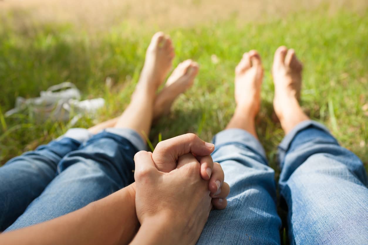 A loving couple laying on the grass holding hands.