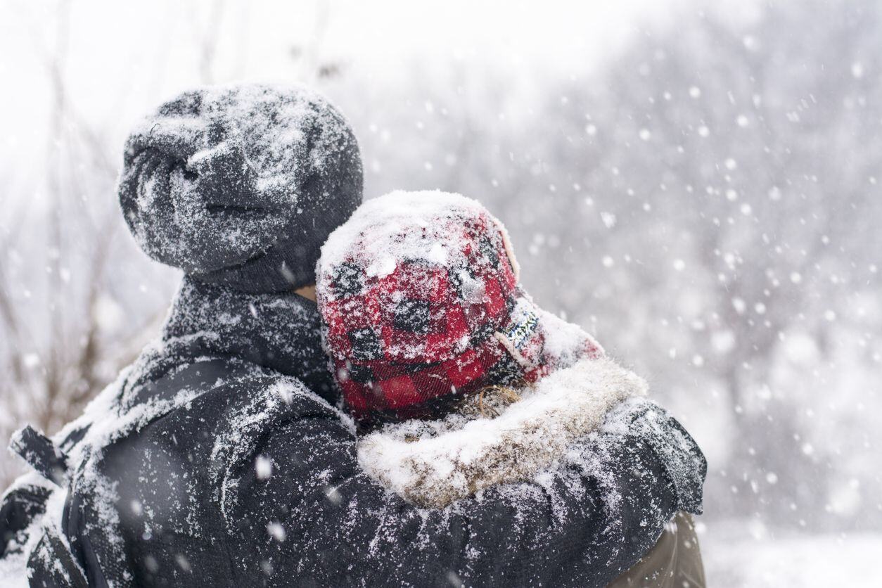 A couple in love outdoors hugging on a winter day with snow falling on them..