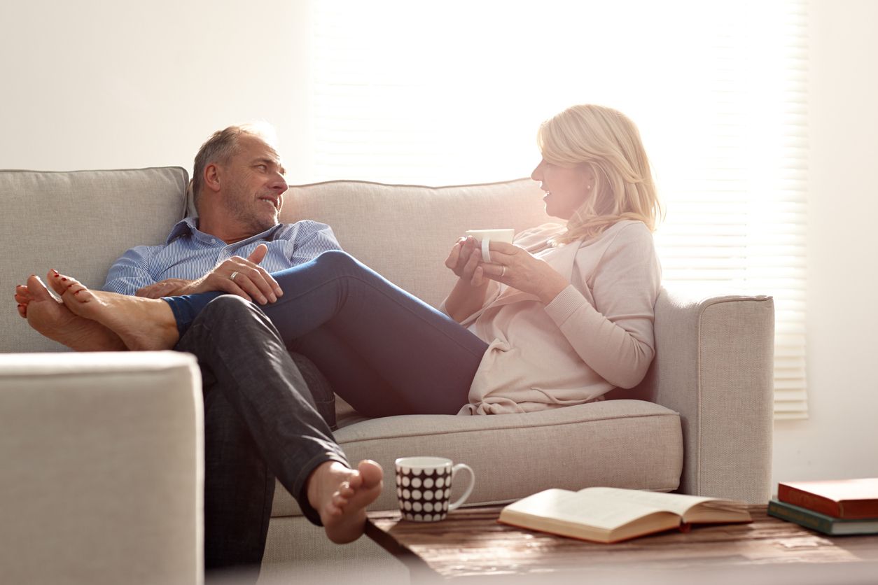A middle-aged, loving couple talking in the living room over coffee.