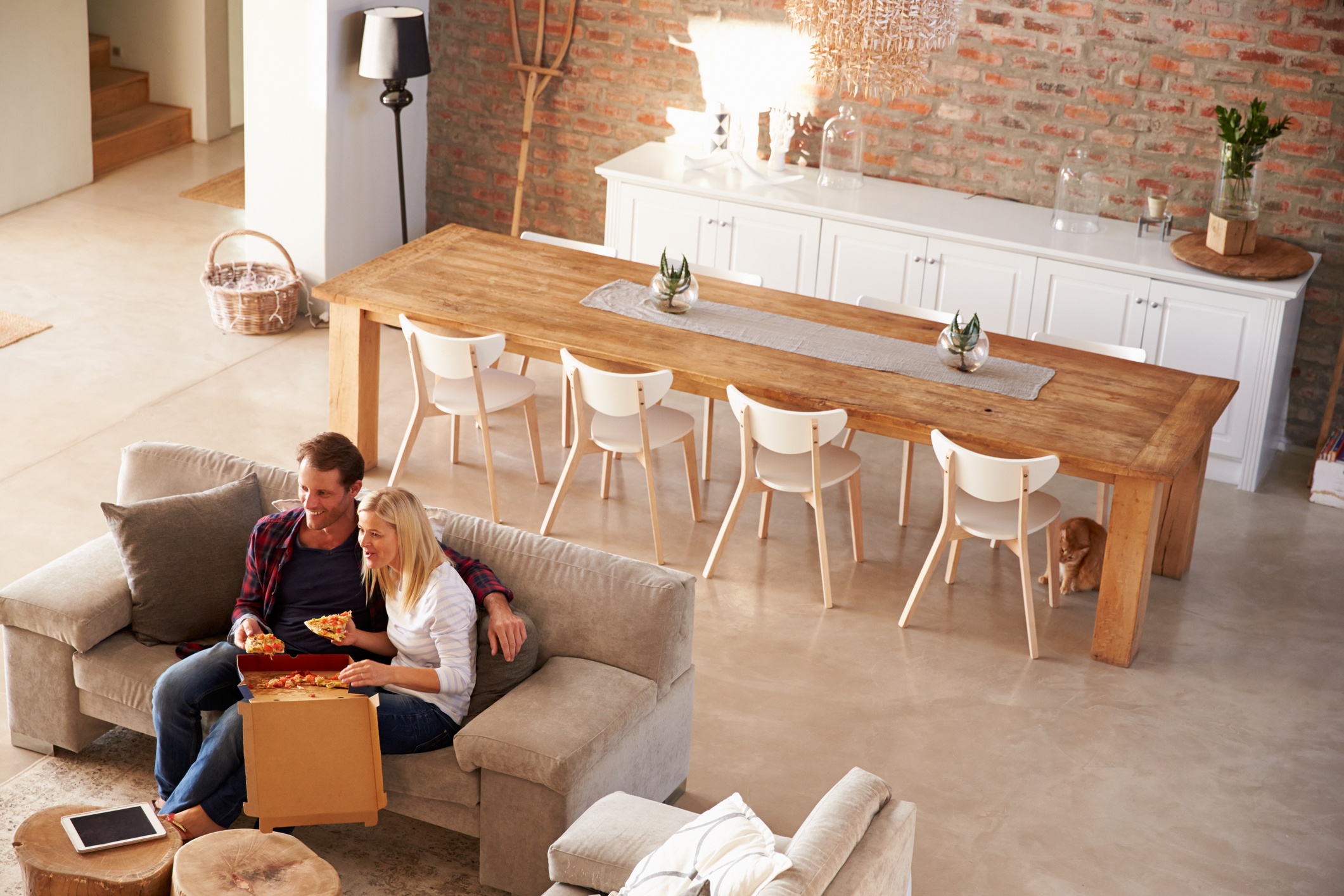 An aerial view of a couple sitting in the living room eating pizza.