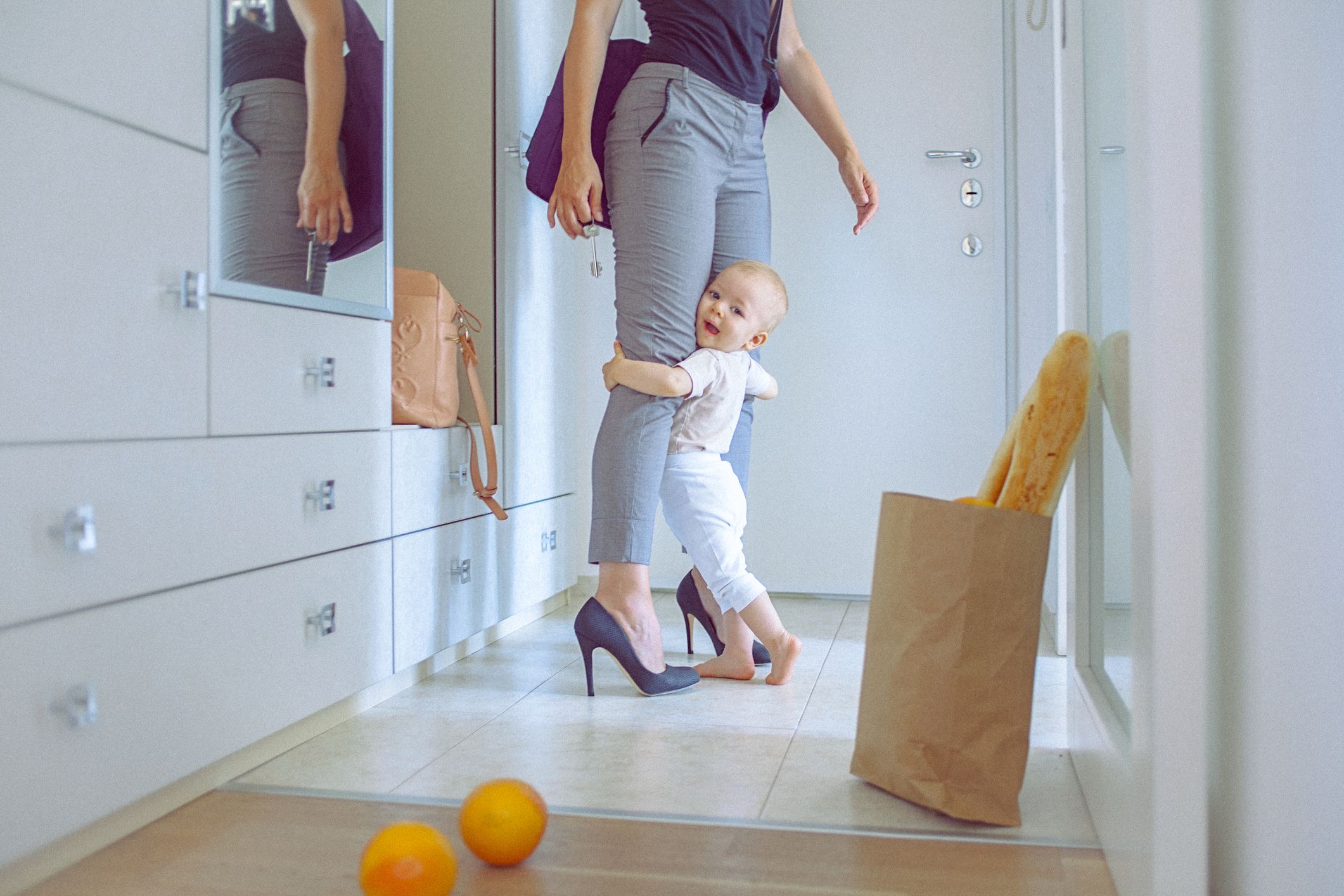 An upset toddler clinging to a mom's legs