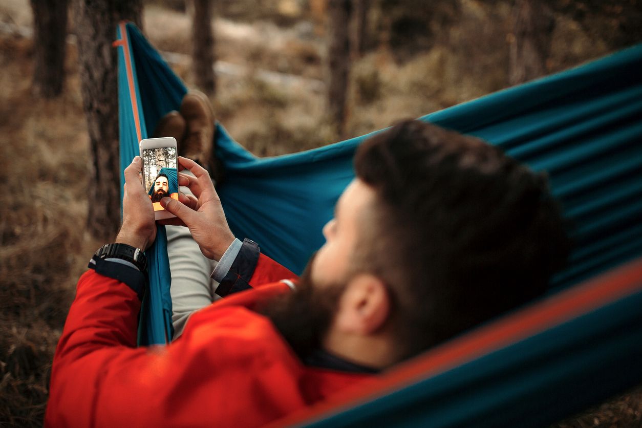 A young man laying in a hammock relaxing on his self-care day in nature.