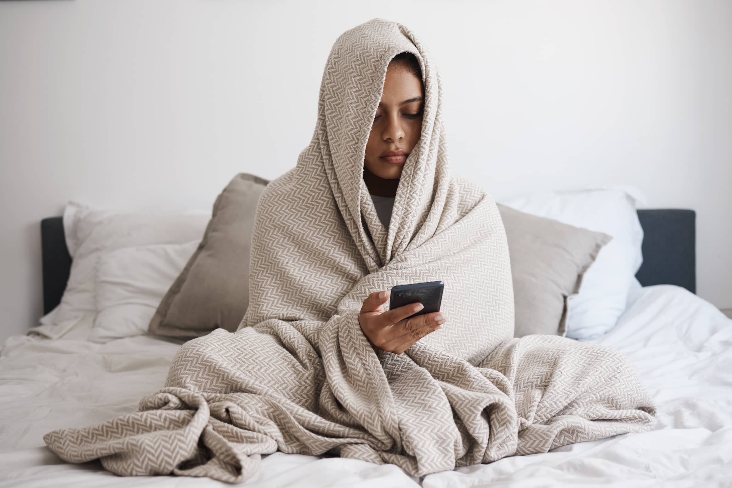 Depressed woman wrapped in blanket sitting on her bed.