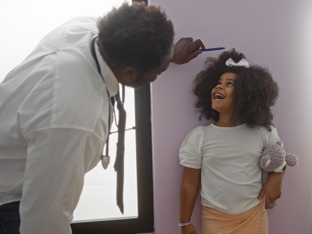 A doctor measuring the height of a smiling child in a health clinic.