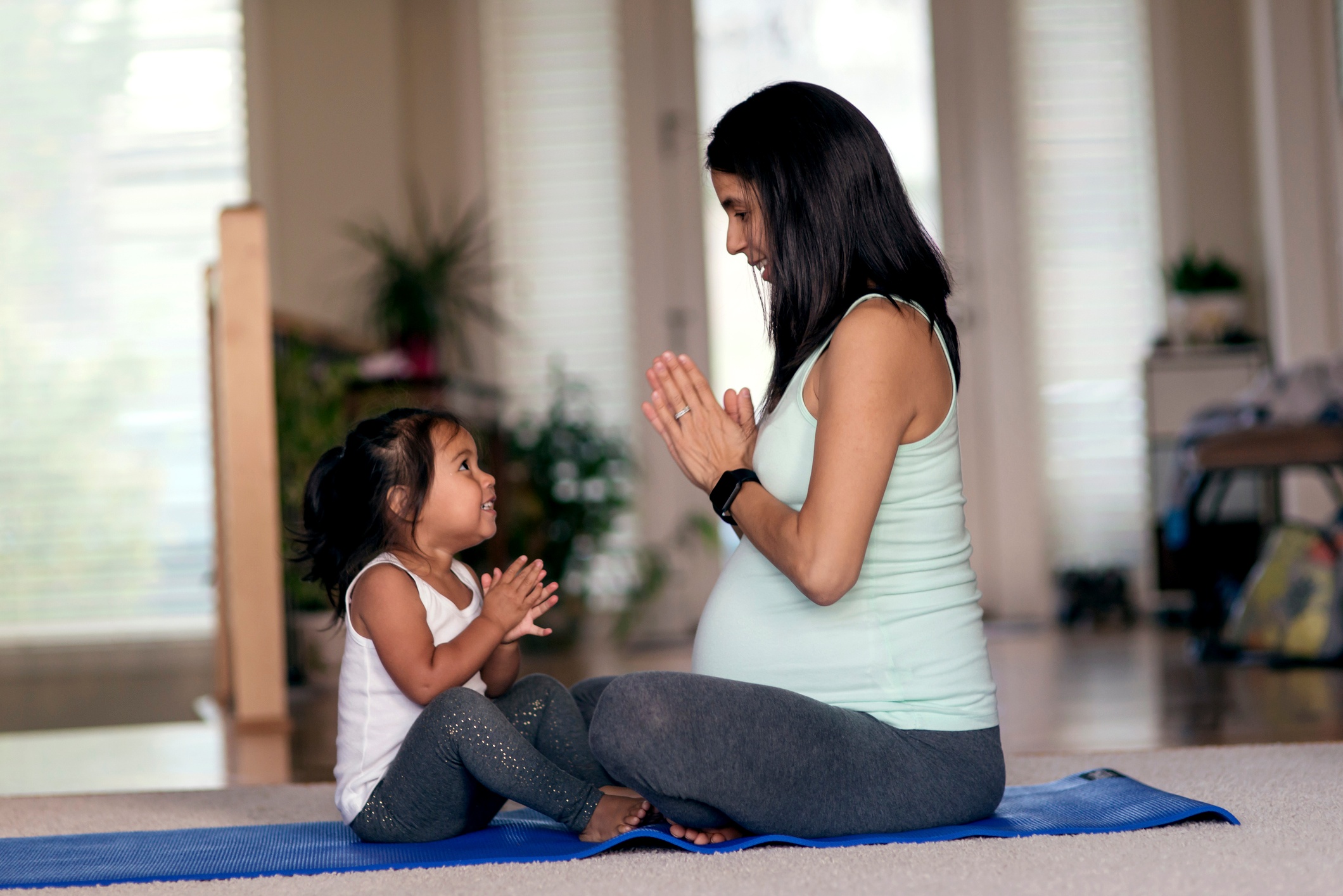 A mother and her 4-year-old daughter meditating together on a blue yoga mat.