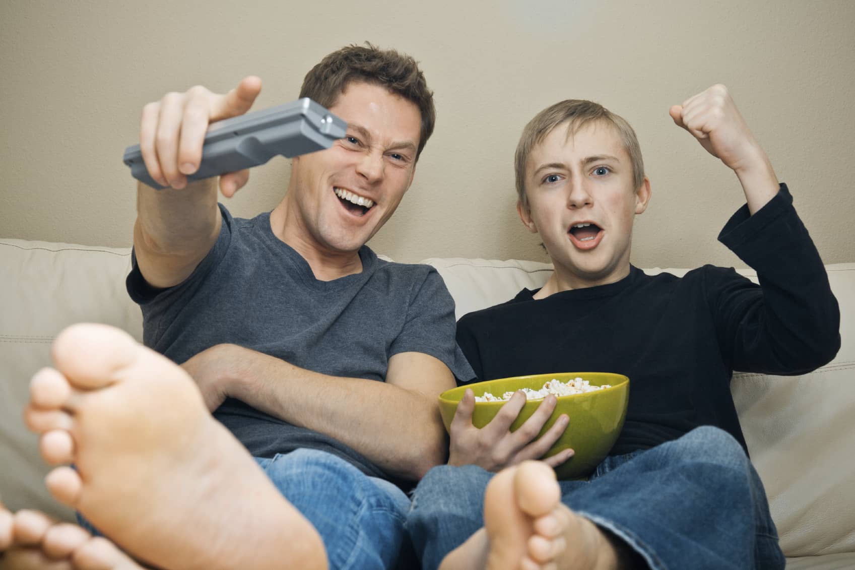 A father and his teenage son watching football excitedly.