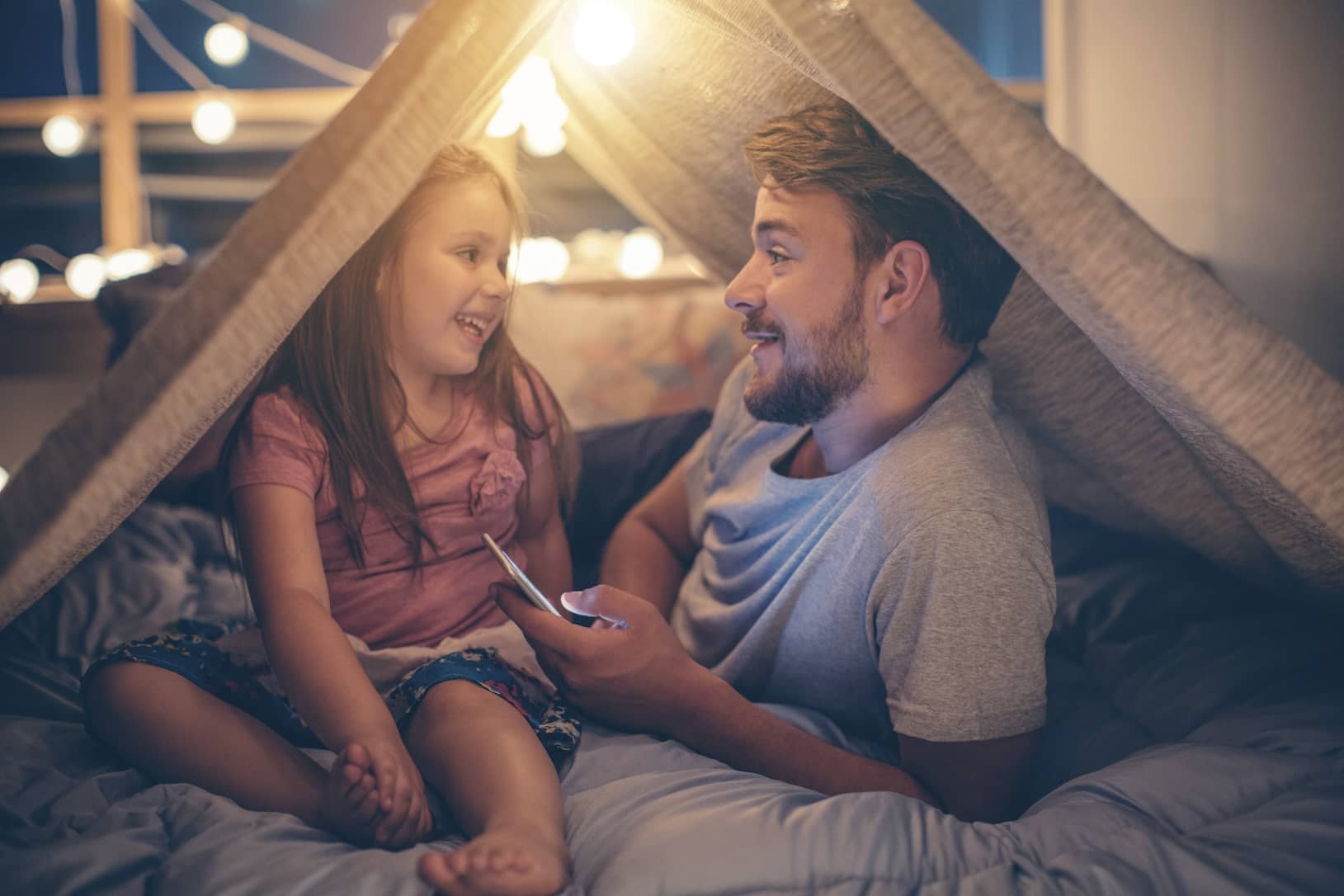 Father and daughter enjoying time under a homemade tent at home.
