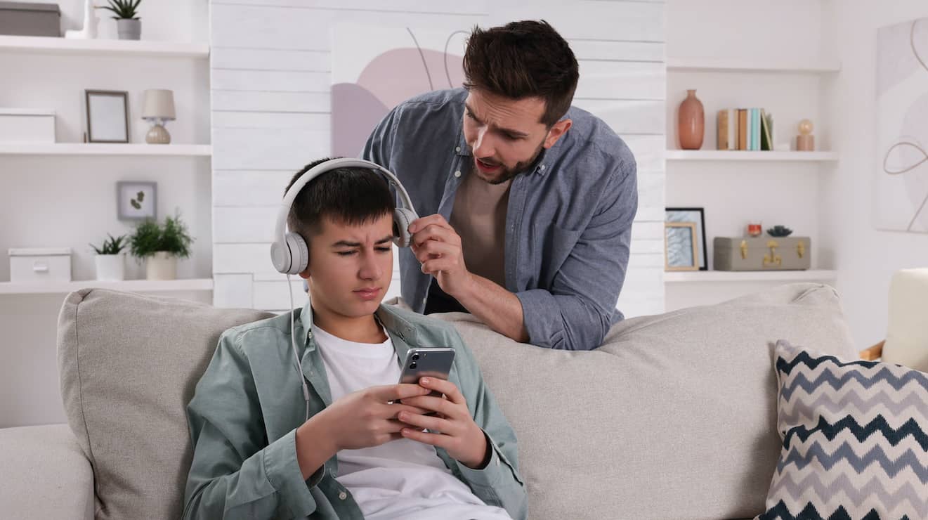 A teen boy in headphones ignores his concerned dad, a common scene in teenagehood conflict.