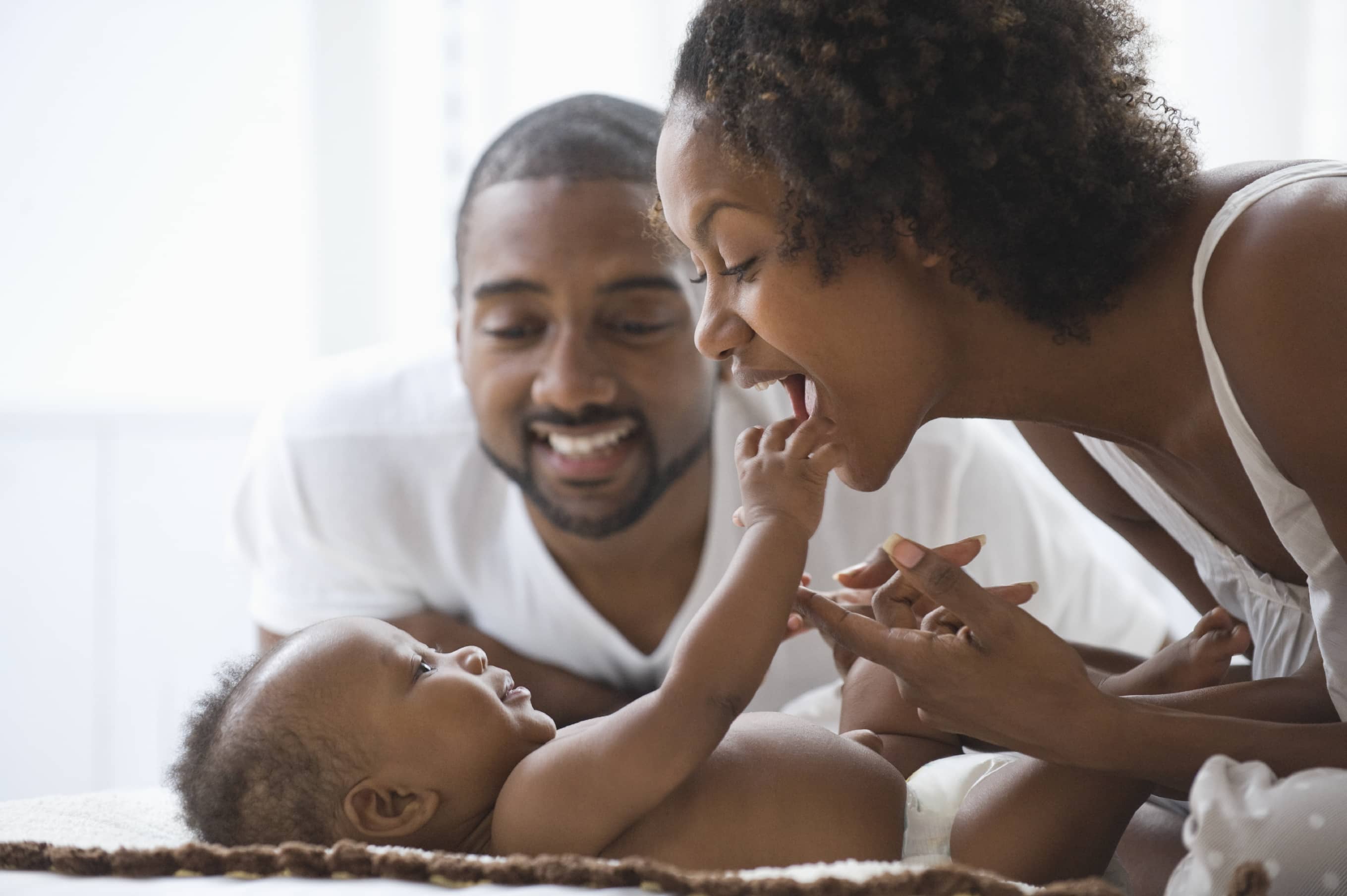 A young black father watching his wife play with their baby boy.