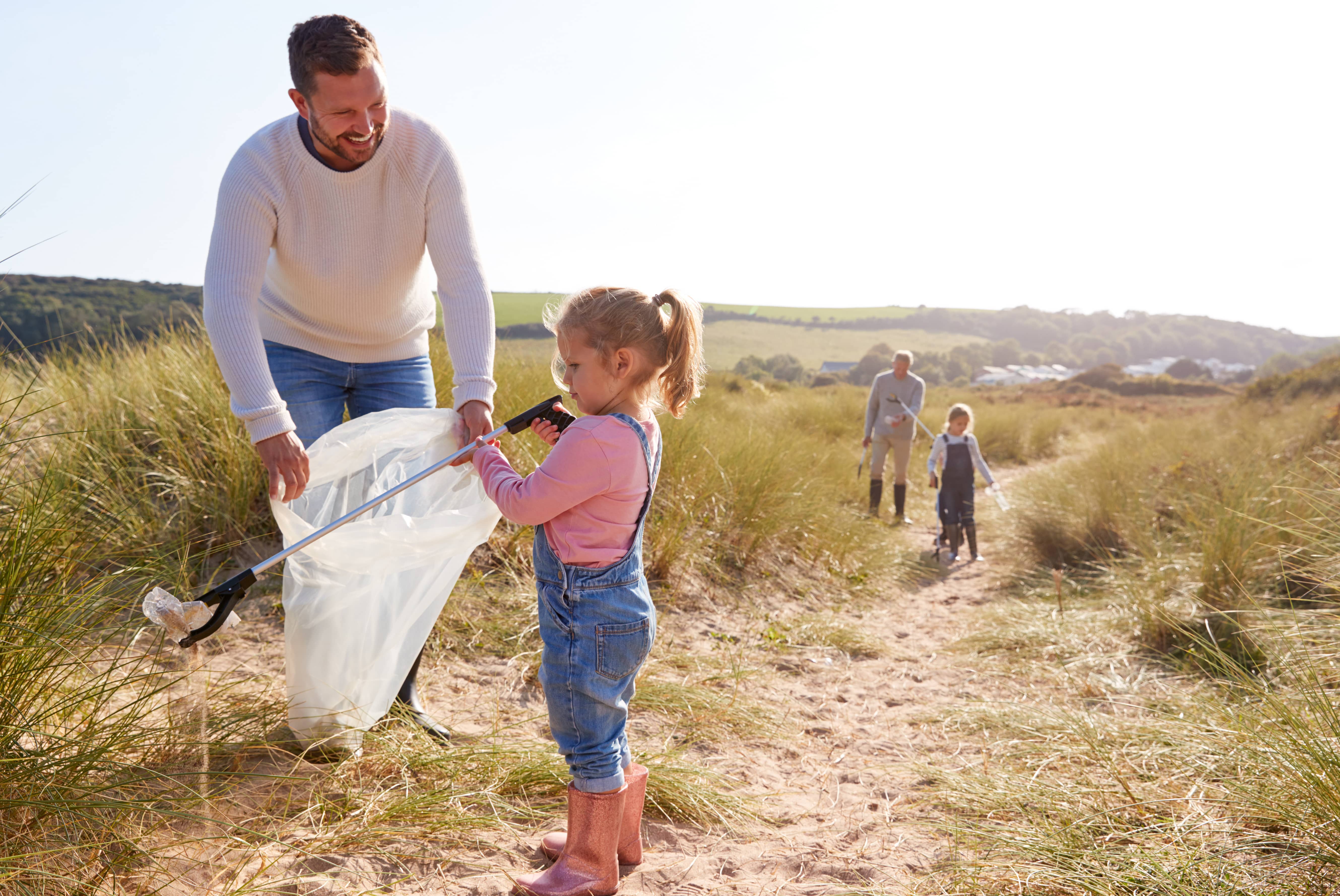 Father with his preschool daughter picking up trash teaching social responsibility.